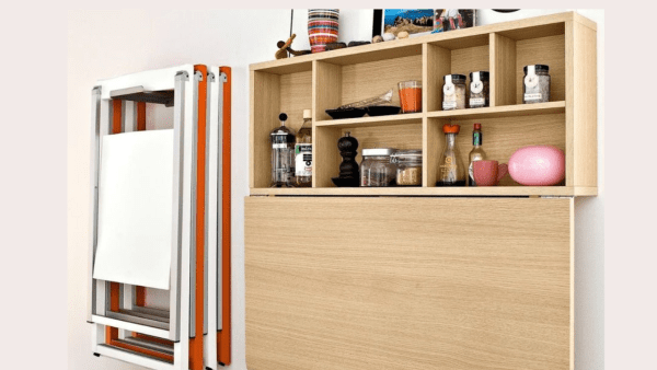 Small kitchen with shelf, refrigerator, and wall mounted table.