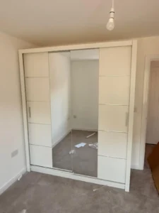 Oslo Sliding Mirror Wardrobe 180cm in White with three panel sliding doors and central mirror, installed in a bedroom. Delivered by Climax Furniture UK (1)